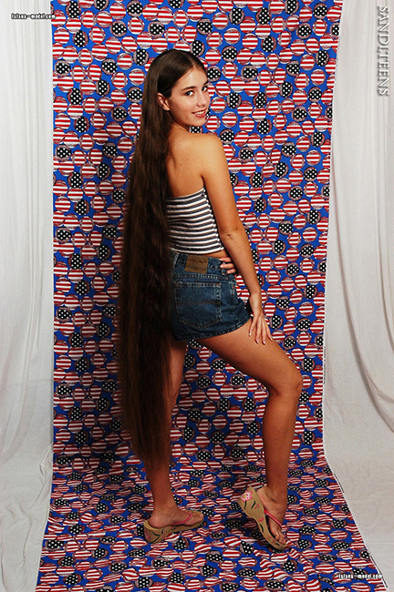 teen female model wearing turquoise top, black skirt and barefooted showing her very long brown hair posing beside the pool