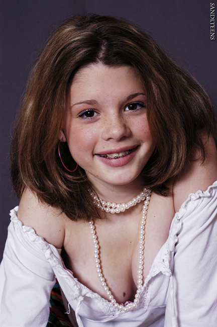 smiling teen female wearing braces, a pixie cut, hoop earings, a pearl mecklace and a peasant blouse showing d�colletage